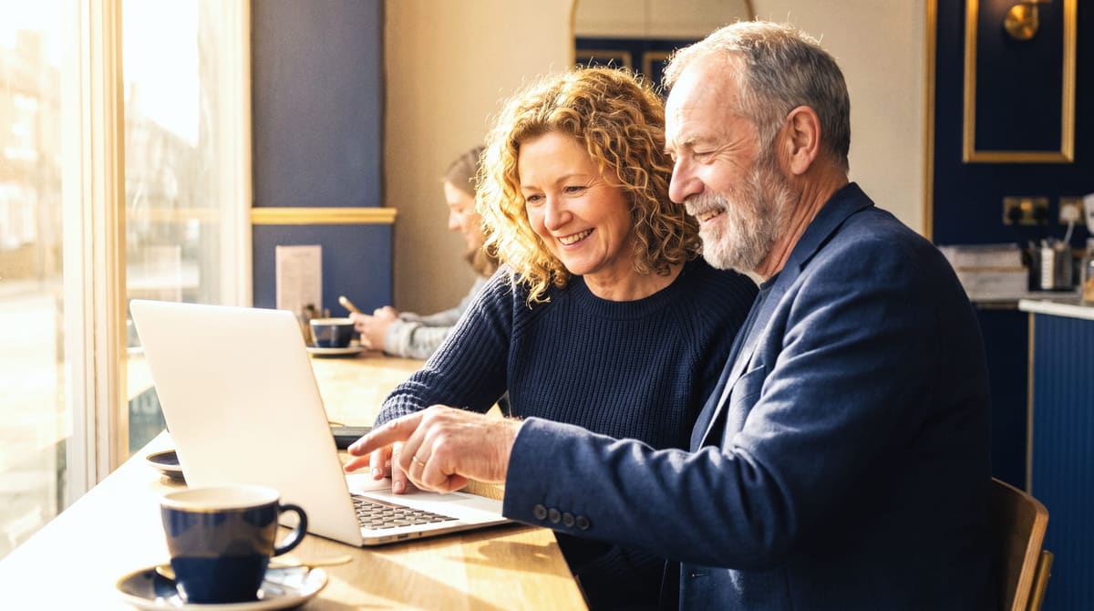 An advisor and a woman in her fifties reviewing options together on a laptop at a bright café table