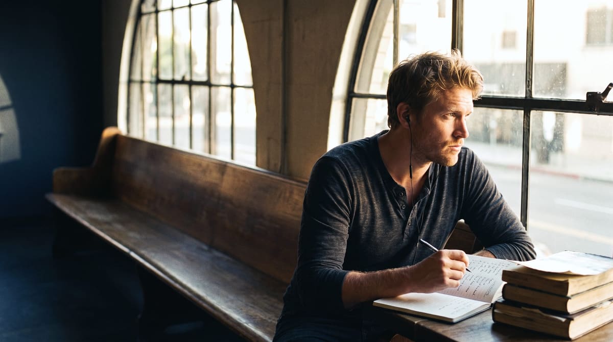A man working alone at a window bench with his books and notes, focused and self-reliant
