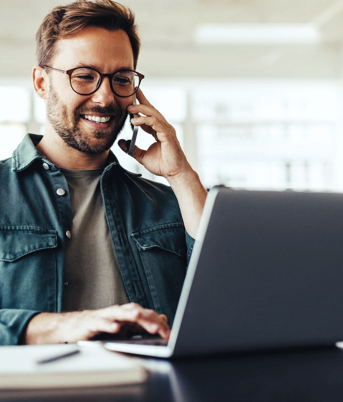 A man smiling on a phone call at his laptop